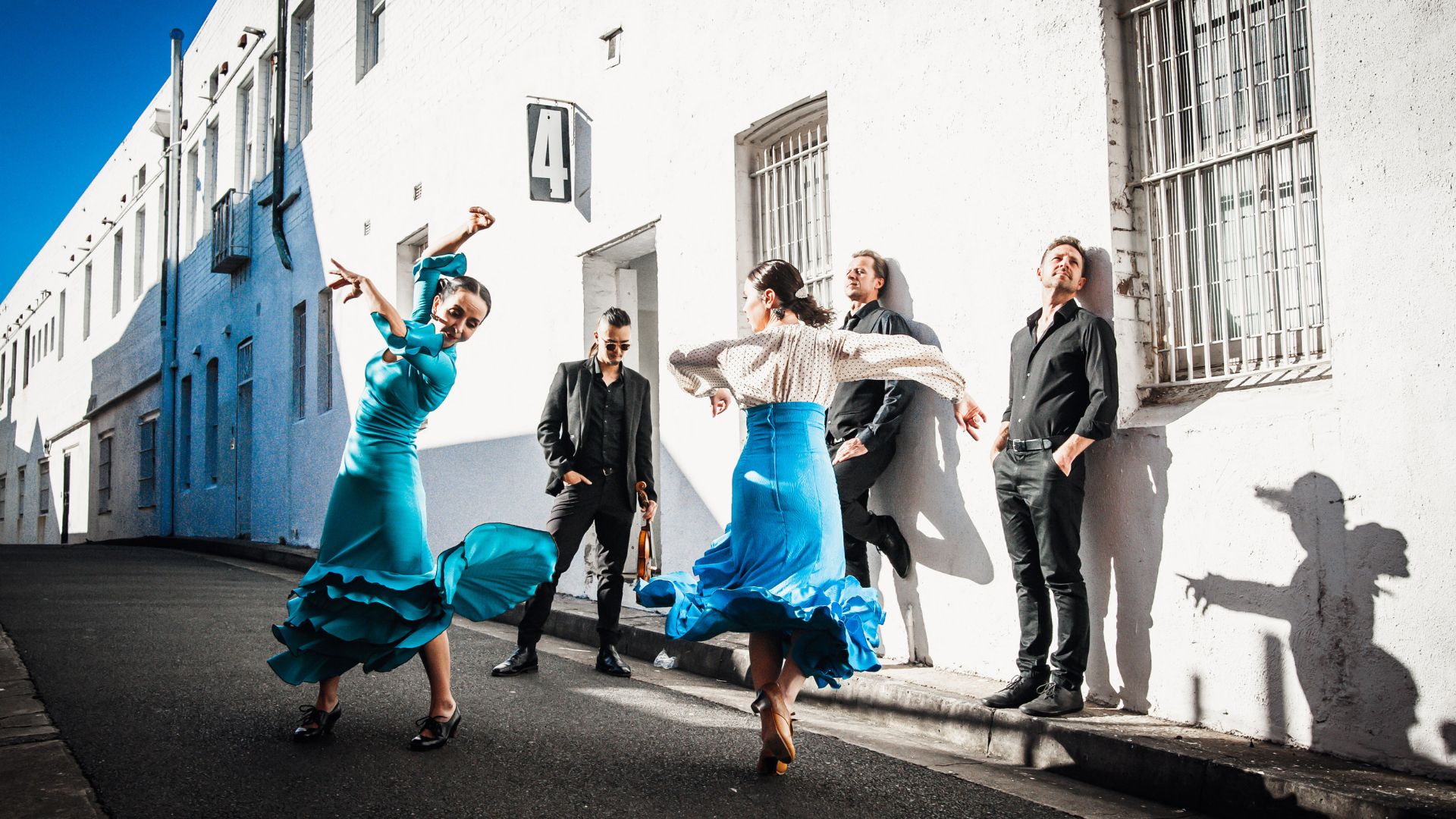 Group of contemporary flamenco dancers in vibrant and fresh blue and white. Dancing in the street.
