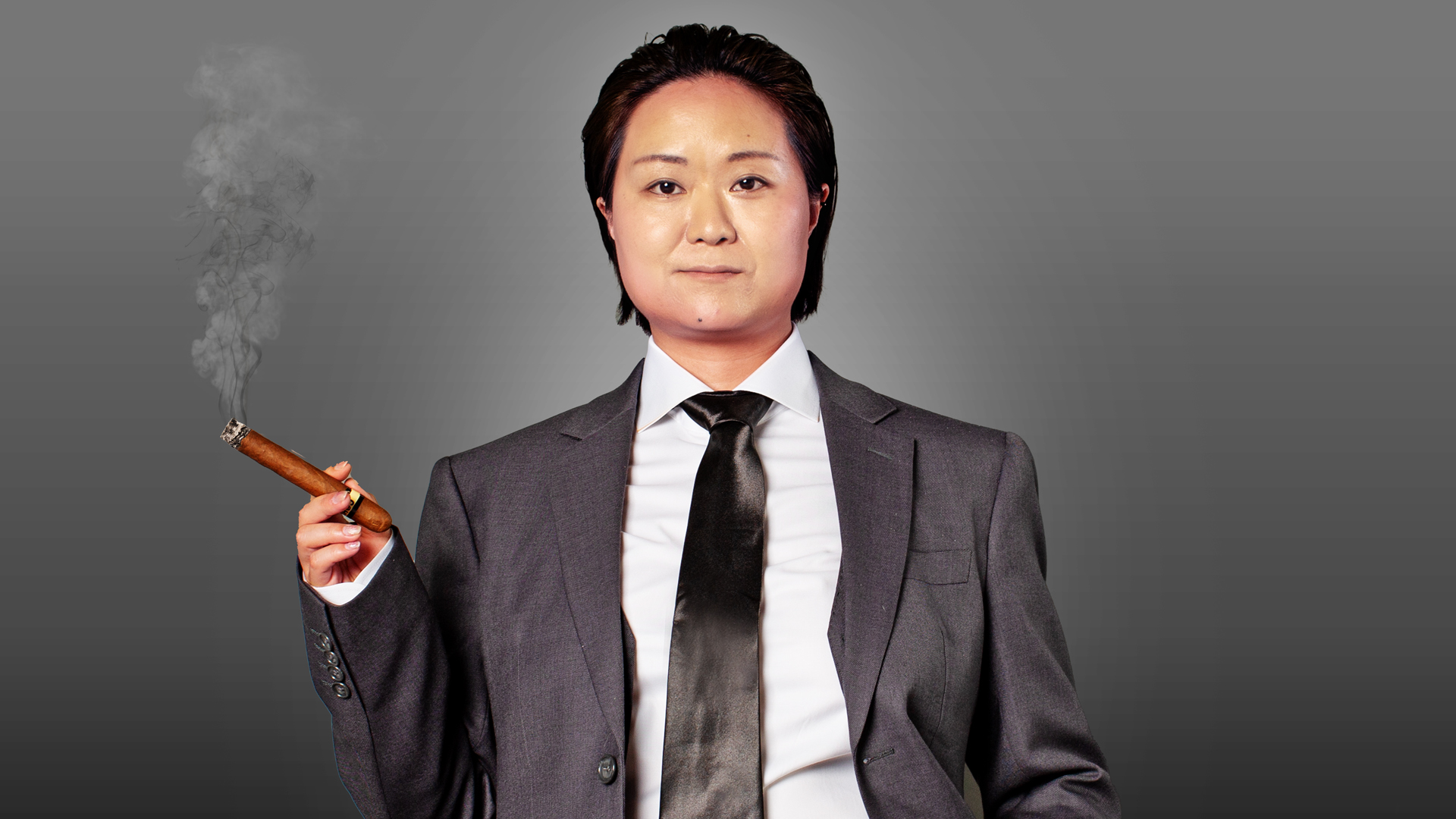 He Huang, with short dark hair and a composed demeanor, stands against a gray backdrop. Dressed in a suit with a white shirt and black tie, he holds a lit cigar as smoke gently ascends—a scene reminiscent of his charismatic presence.