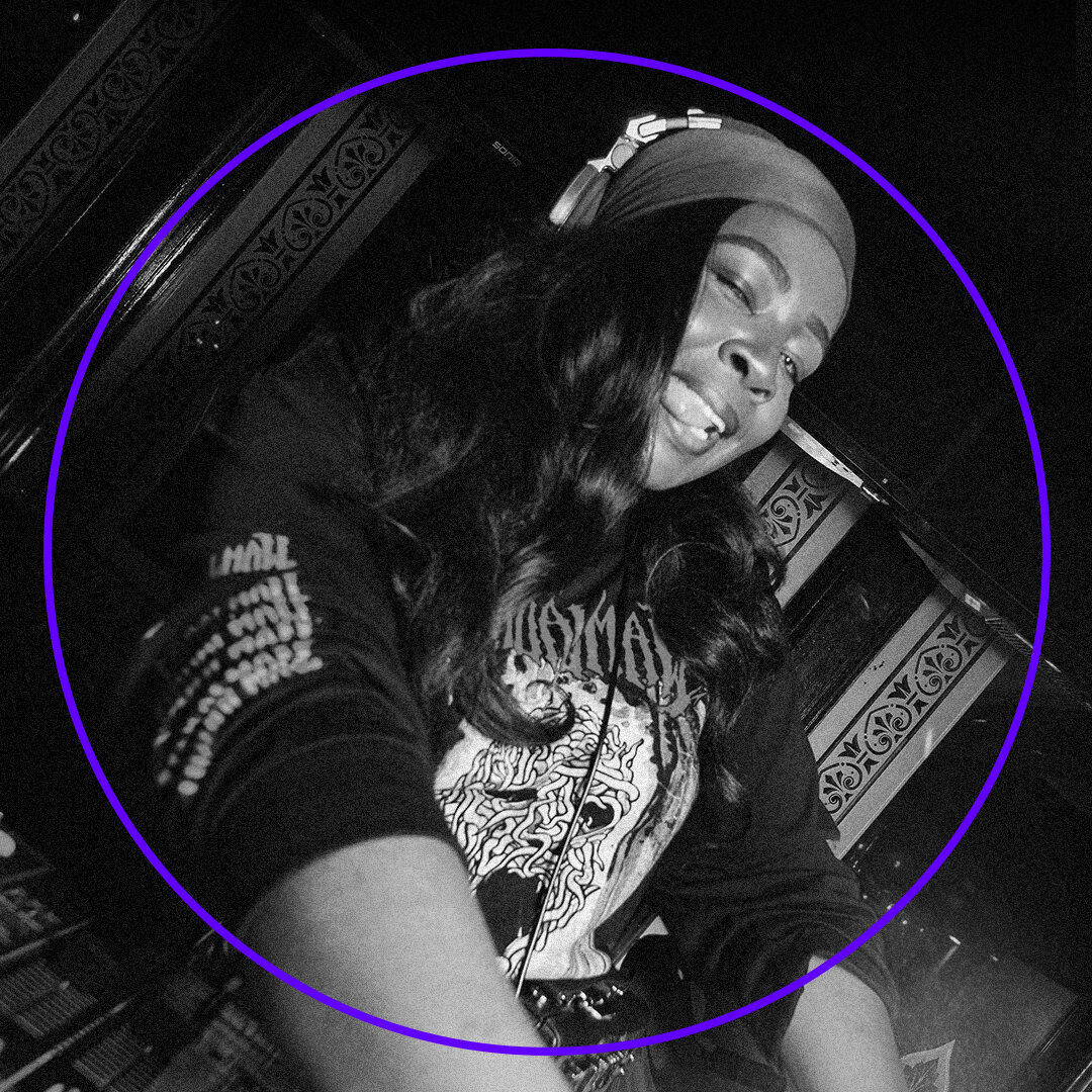 A DJ wearing a beanie and headphones is smiling while spinning tracks at the OHM Festival 2025. The black-and-white image with a purple circle highlighting the DJ captures the vibrant energy of Brisbane Powerhouse, adorned with intricate wall patterns.