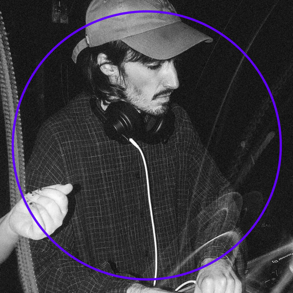 A DJ wearing a cap and headphones is focused on mixing at a DJ console, surrounded by a purple circle. A persons hand gestures towards him against the lively backdrop of the OHM Festival 2025. The black and white image captures the electric ambiance of a Silent Disco at Brisbane Powerhouse.