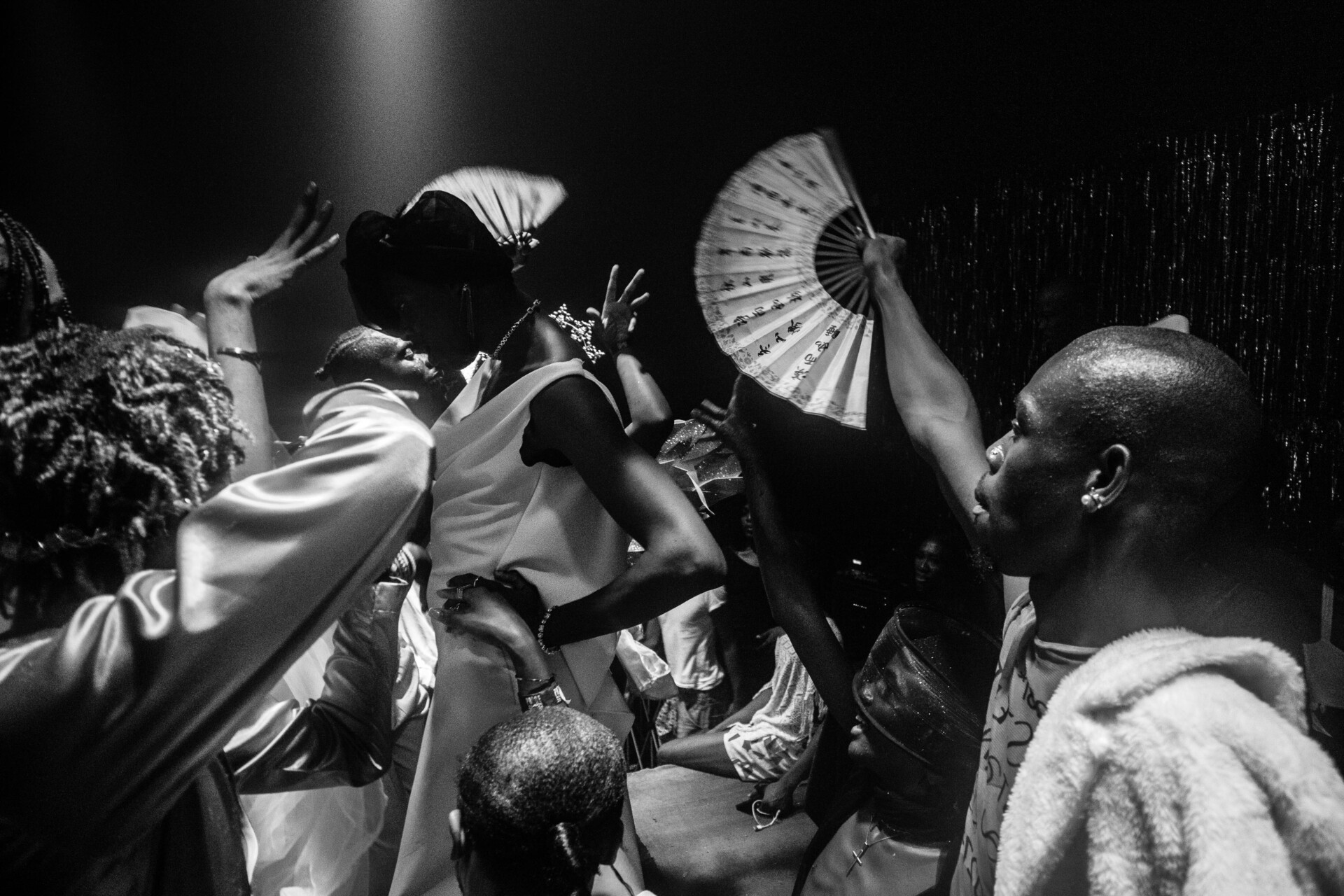 A black and white photo shows a lively crowd dancing and waving fans, with a spotlight highlighting a central figure in a dress and headscarf—one of many powerful moments captured at the World Press Photo Exhibition 2025 Brisbane Powerhouse.