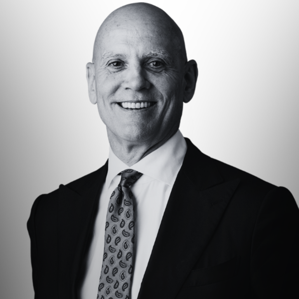 A bald man in a suit and patterned tie smiles at the camera against a plain, light background, representing Our Team - Brisbane Powerhouse.