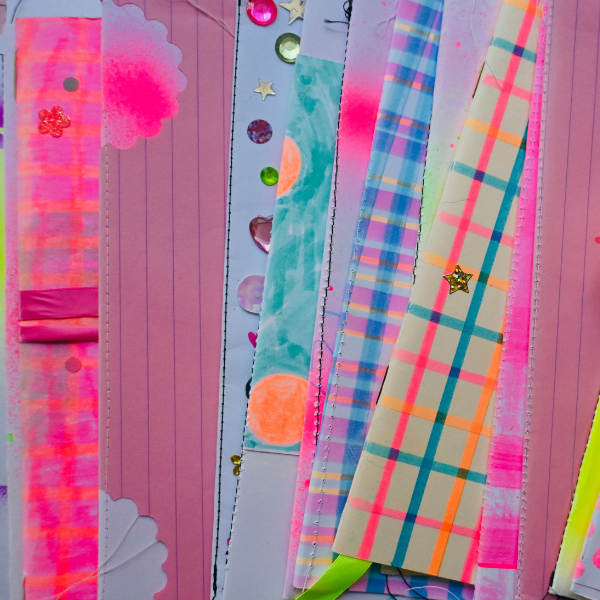 A colorful collage of papers featuring pink, plaid, and pastel patterns, neon highlights, and shiny decorations like sequins and stars, all layered closely together.