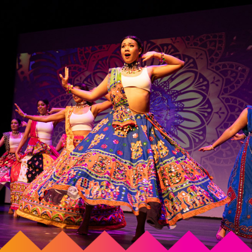 A group of women perform a traditional Indian dance on stage, wearing colorful, patterned skirts and white tops. LED HULA HOOPS light up the vibrant mandala backdrop at Ubuntu Social, Brisbane Powerhouse, enhancing the festive atmosphere.