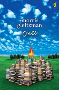 Book cover for Once by Morris Gleitzman. The image shows stacks of books on green grass under a blue sky; in the background, more books burn in a fiery blaze, with trees lining the horizon.