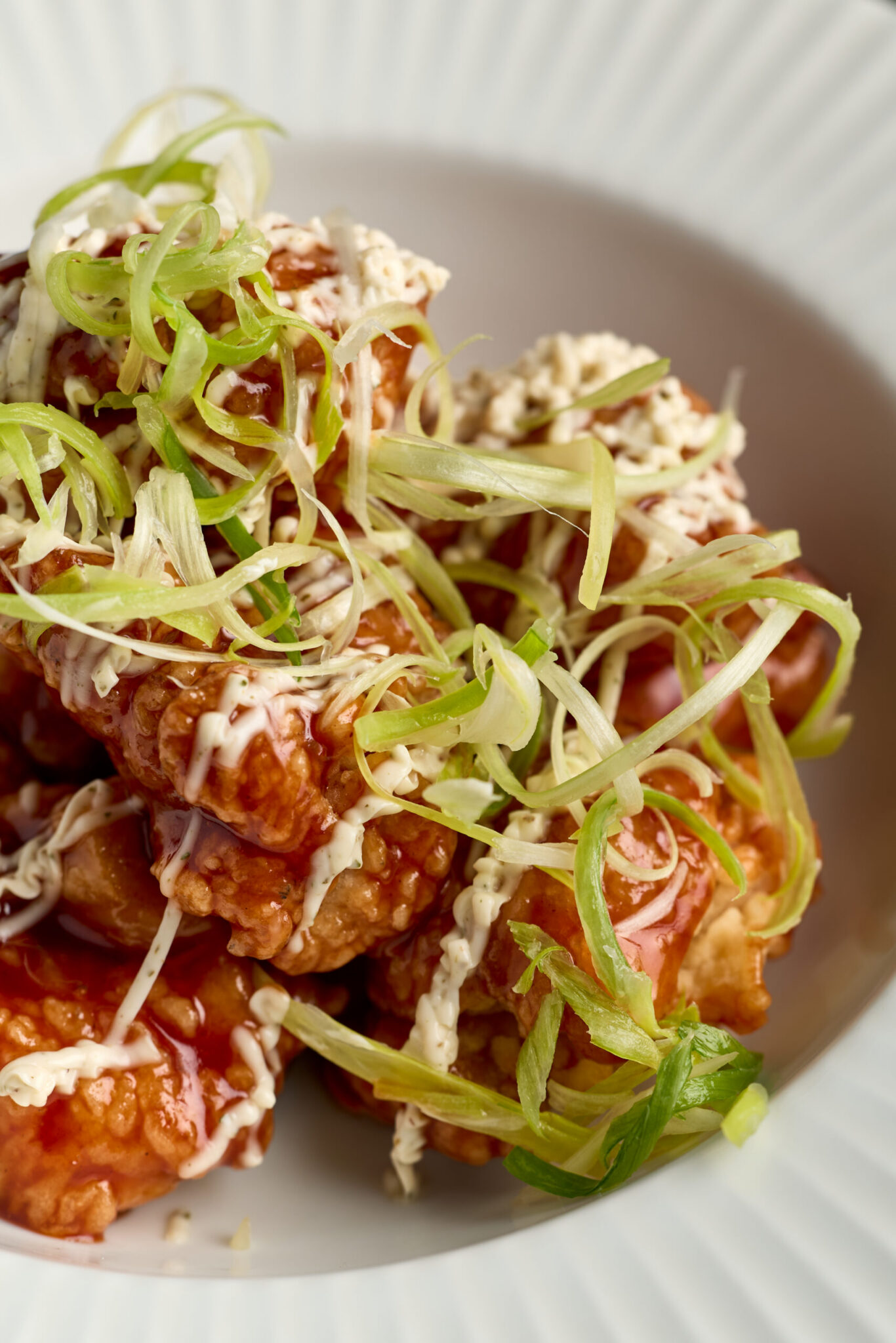 A close-up of crispy fried chicken pieces drizzled with creamy sauce and topped with thinly sliced green onions, served in a white bowl at Night Feast 2026 Brisbane Powerhouse.