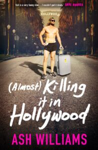 A muscular man in black shorts stands confidently on a Hollywood street with palm trees, holding sunglasses and a suitcase. The book title (Almost) Killing it in Hollywood by Ash Williams is written in bold, playful text.