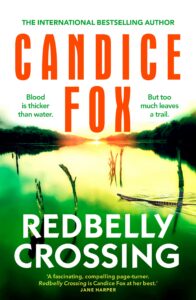 Book cover for Redbelly Crossing by Candice Fox, featuring a bright river scene with green and yellow hues, sun setting, and two wooden logs in the water; text includes praise and tagline about blood and trails.