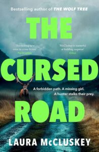 Book cover for The Cursed Road by Laura McCluskey. A deer stands on a misty, deserted road flanked by grass, with large green title text overlaying the image.
