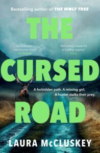Book cover for The Cursed Road by Laura McCluskey, featuring a large stag standing on a misty, muddy path with mountains in the background and bold green text over the image.