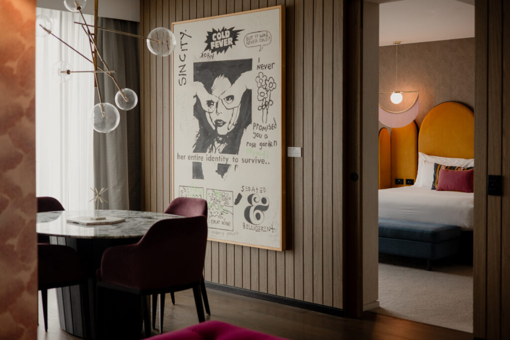 A large framed black-and-white graphic art piece that invites visitors to Brisbane Powerhouse, hanging on a wood-paneled wall between a dining area and a bedroom.