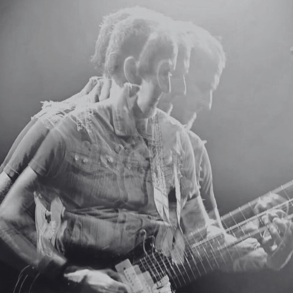 A double-exposure black and white photograph of a guitarist playing on stage.